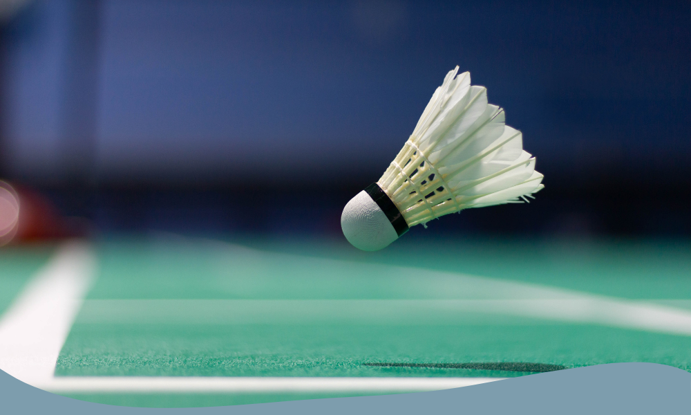 Flygande badmintonboll över en grön badmintonbana under pågående spel.