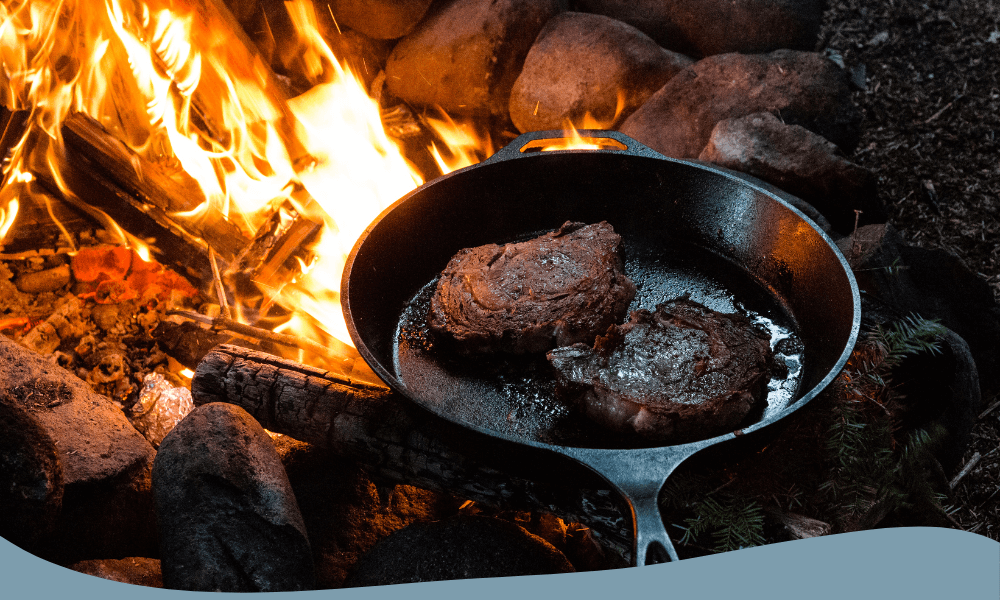 Stekande kött på gjutjärnsstekpanna över öppen eld, perfekt för campingmatlagning