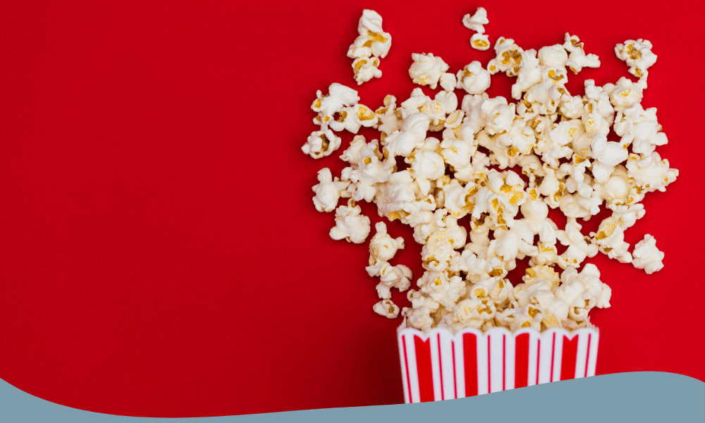 Färska popcorn som hälls ur en röd och vit pappförpackning mot en röd bakgrund