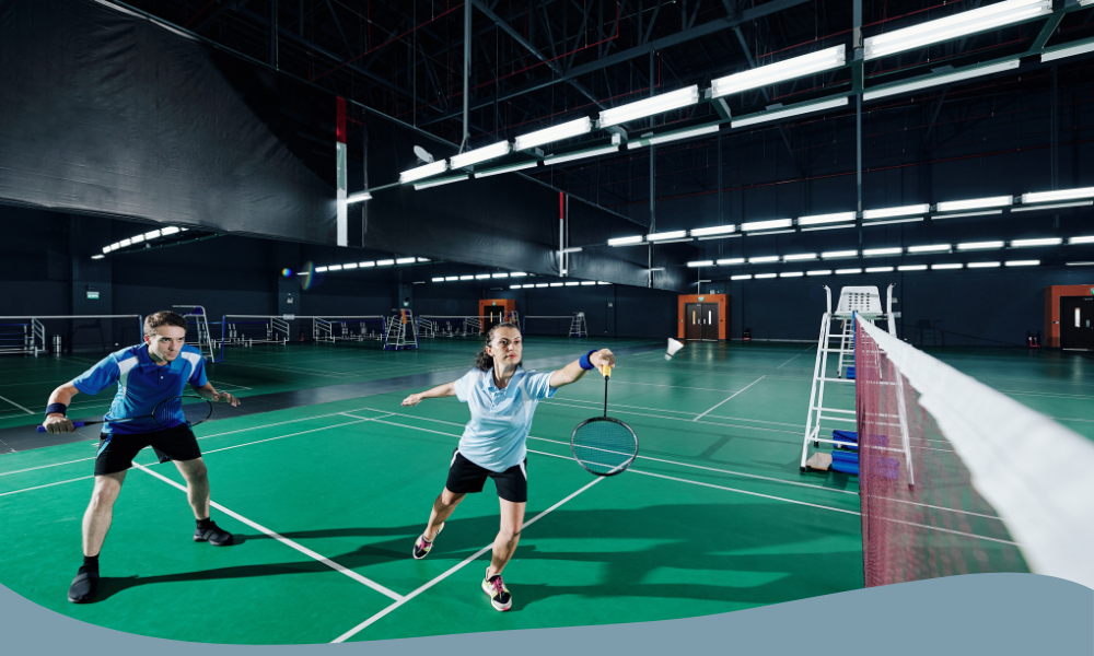 Två spelare i dubbelmatch på badmintonbana inomhus under intensivt spelmoment.