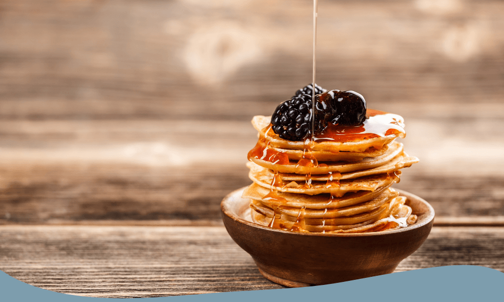 Hög med små pannkakor toppade med björnbär och sirap i träskål