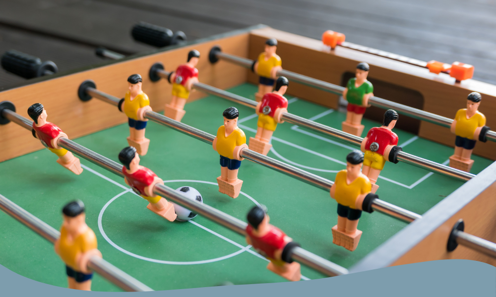 Närbild på fotbollsspel med spelare i rött och gult, realistiskt spelplan för bordfotboll hemma.