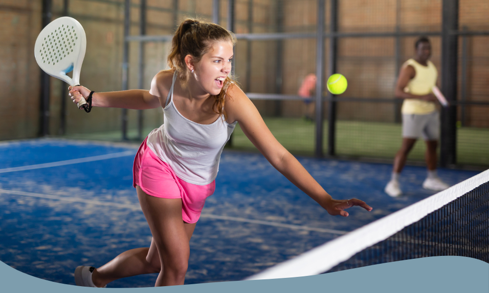 Kvinna i vit topp och rosa shorts spelar padel och slår volley vid nätet