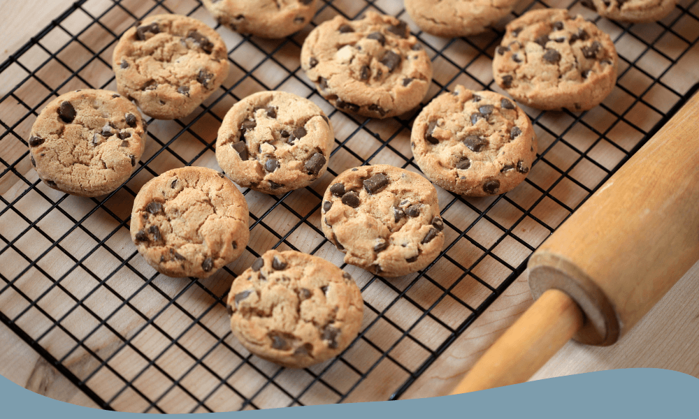 Nybakade chocolate chip cookies på ett avsvalningsgaller bredvid en kavel