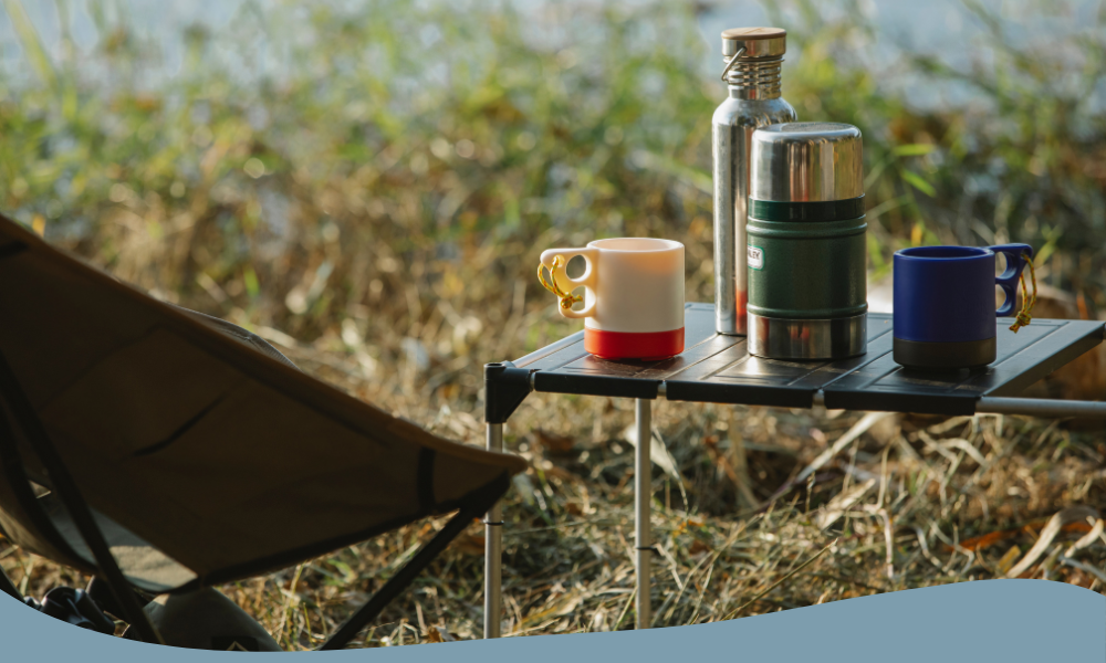 Campingbord med termosar och färgglada muggar – redo för en varm dryck ute i naturen.