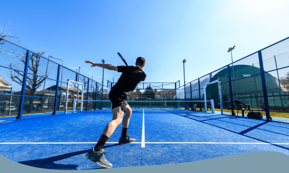 Man utför ett kraftfullt slag under en padelmatch på en utomhusbana med blått underlag.