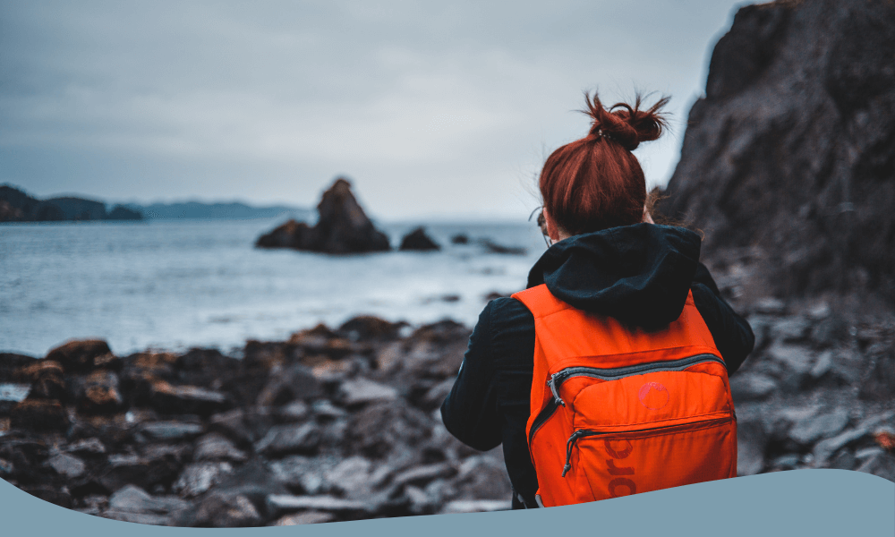 Kvinna med röd ryggsäck för vandring vid klippig kust, idealisk för längre dagsutflykter med packning.