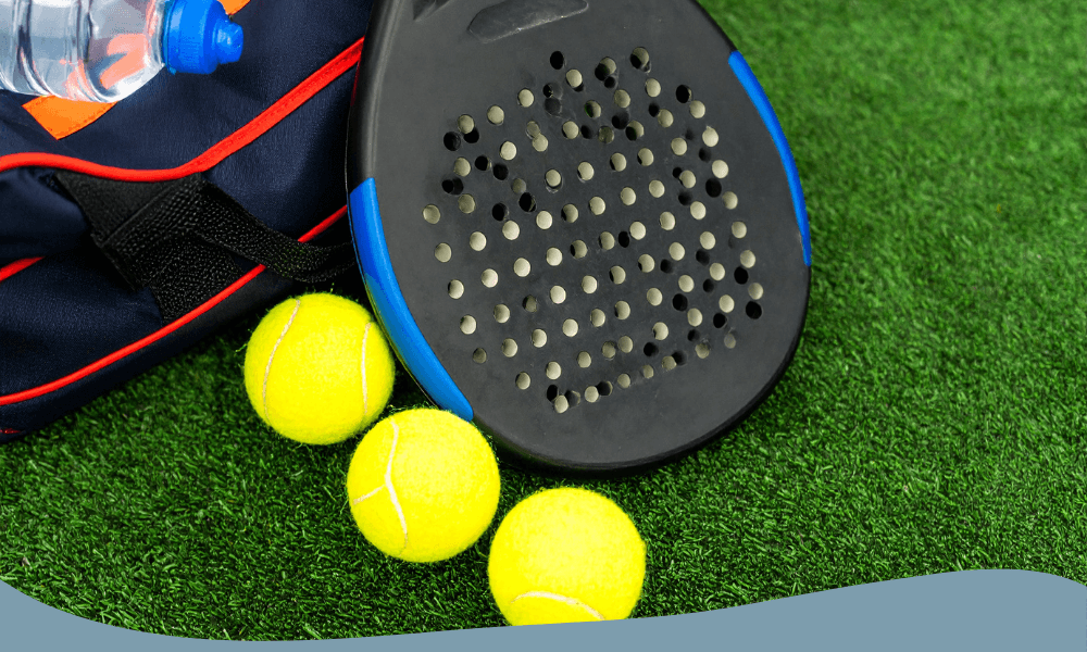 Padelracket med blå detaljer placerad bredvid tre gula padelbollar.