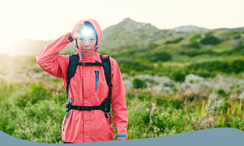 Kvinna med pannlampa i regnjacka under friluftsaktivitet i gryning eller skymning.