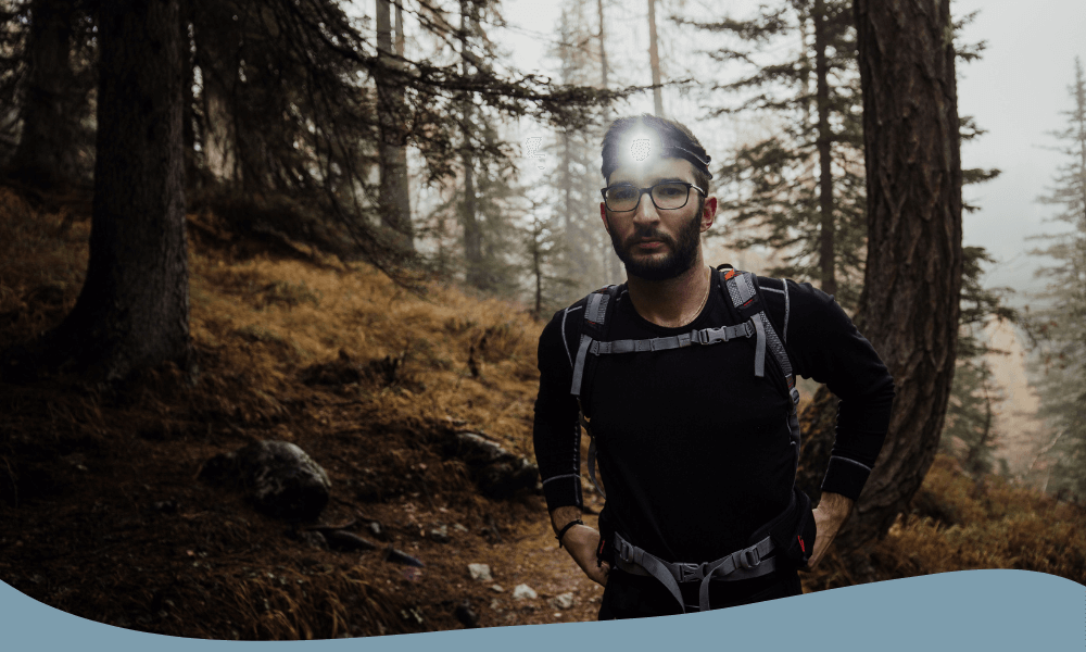 Man med pannlampa som lyser starkt under en vandringstur i skogen.